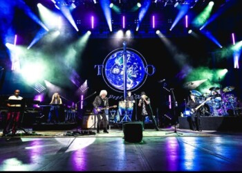 Live band performing on stage with vibrant lights and large circular screen.