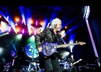 Guitarist performs on stage with vibrant colorful lights.