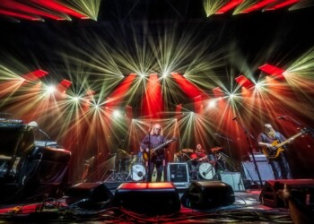 Warren Haynes Christmas Jam 2025 A guitarist performs on stage under vibrant red and yellow lights.