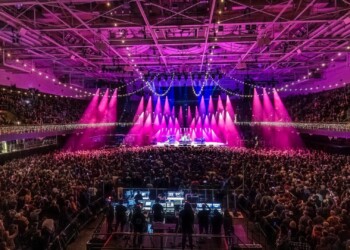 Warren Haynes Christmas Jam 2025 A large crowd enjoys a colorful concert with vibrant stage lighting.