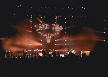 Concert stage with 'Zaca Tap' sign and bull skull logo, lit in warm orange hues.
