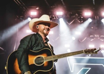 A musician in a cowboy hat playing guitar on stage with bright lights.