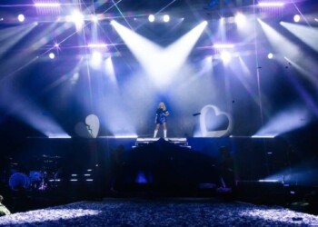 DJ performing on stage with vibrant lights and crowd below.