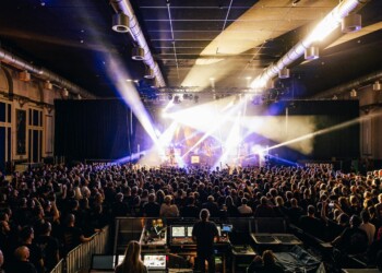 A packed concert venue with bright stage lights and an enthusiastic crowd.