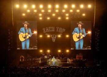 A country singer performs on stage with guitar under bright lights.